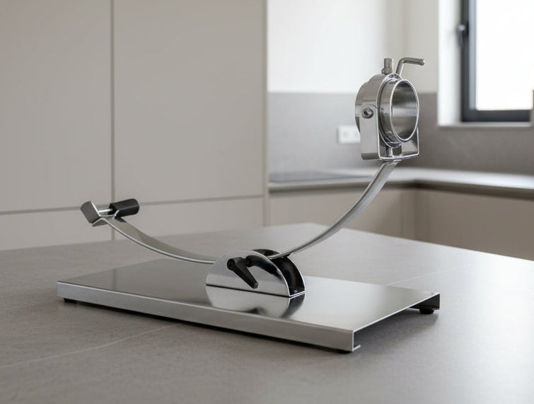 A modern stainless steel kitchen tool with a curved arm and circular component, displayed on a sleek gray countertop in a minimalist kitchen setting.