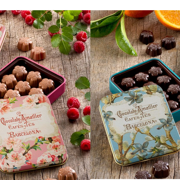 Decorative chocolate tins with floral designs on a wooden surface with fruits.