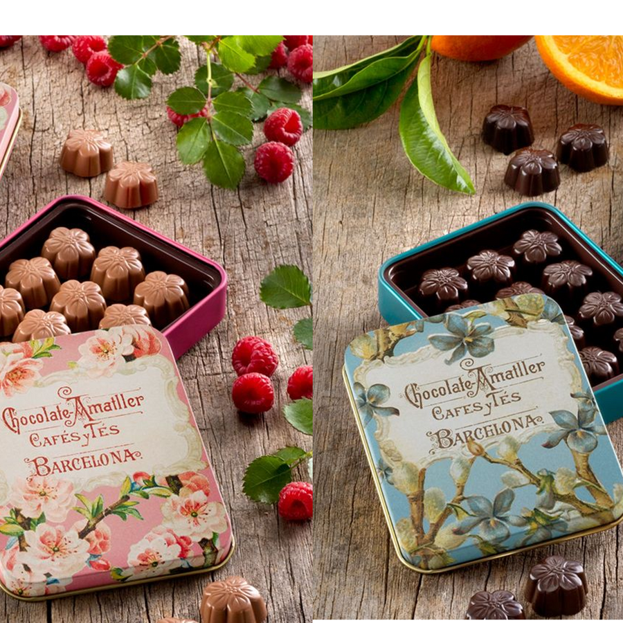 Decorative chocolate tins with floral designs on a wooden surface with fruits.